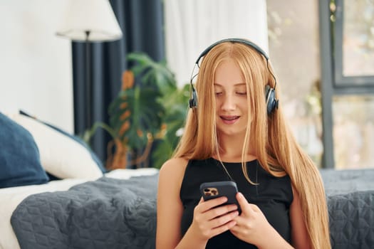 Listening to the music. Female teenager with blonde hair is at home at daytime.