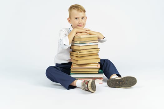 A schoolboy sits near a stack of books with his hands on them. Isolated background. Education concept