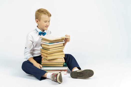 A schoolboy sits near a stack of books and reads. Isolated background. Education concept