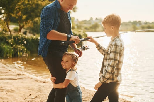 Father with son and daughter on fishing together outdoors at summertime.