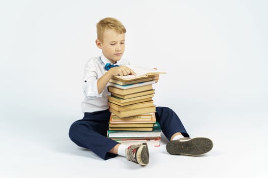 A schoolboy sits near a stack of books and reads. Isolated background. Education concept