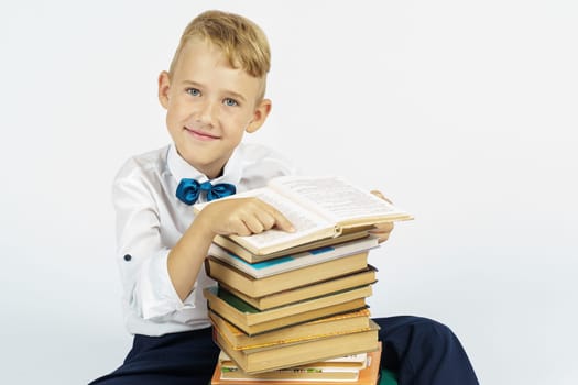A schoolboy is sitting near a stack of books and smiling while looking at the camera. Isolated background. Education concept
