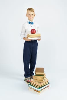 A schoolboy stands near a stack of books, holding books and an apple in his hands. Isolated background. Education concept