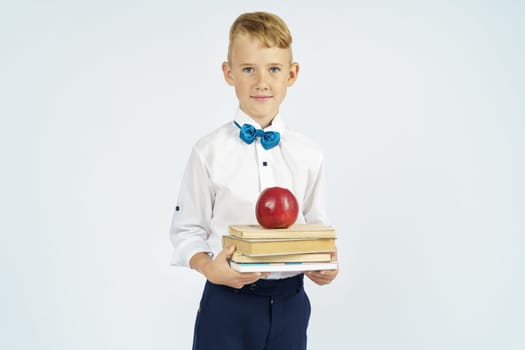 The schoolboy holds books and an apple in his hands. Isolated background. Education concept