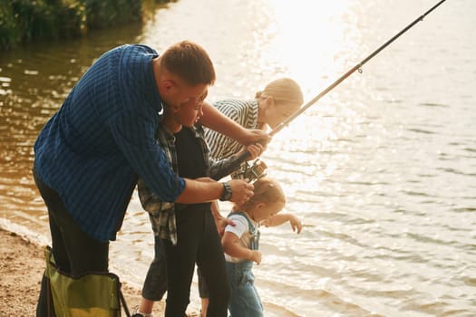 Learning to fishing. Father and mother with son and daughter together outdoors at summertime.