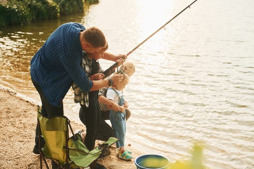 Learning to fishing. Father and mother with son and daughter together outdoors at summertime.