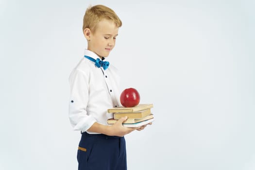 The schoolboy holds books and an apple in his hands. Looks at them. Isolated background. Education concept