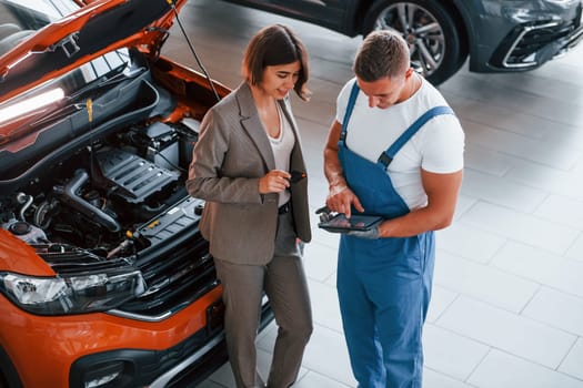 With female customer. Man repairing woman's automobile indoors. Professional service.