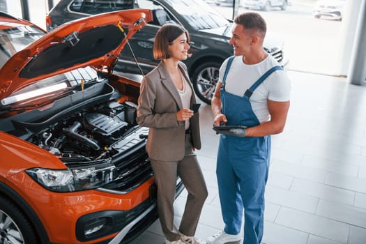 With female customer. Man repairing woman's automobile indoors. Professional service.