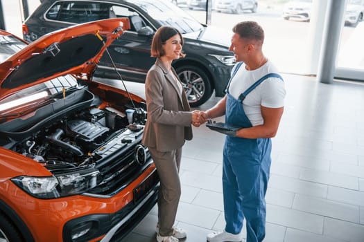 With female customer. Man repairing woman's automobile indoors. Professional service.