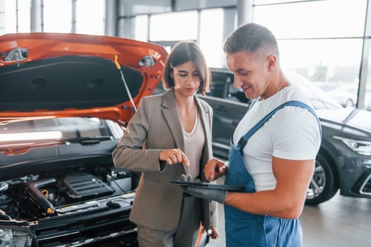 With female customer. Man repairing woman's automobile indoors. Professional service.