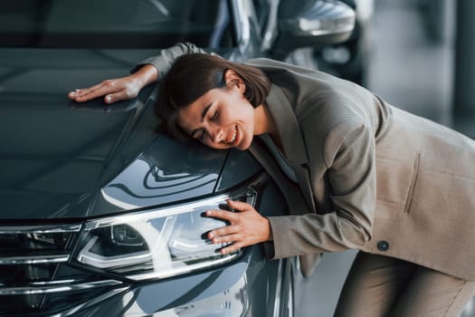 Black colored car. Woman is indoors near brand new automobile indoors.