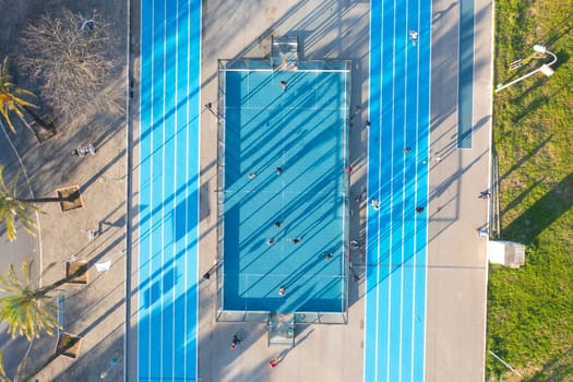 Aerial view of blue running track and multi-sport court in public park. Used to practice football, basketball jogging. Top view. Sunny day. Sunset. Drone photo.