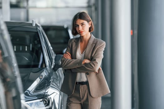 Black colored car. Woman is indoors near brand new automobile indoors.