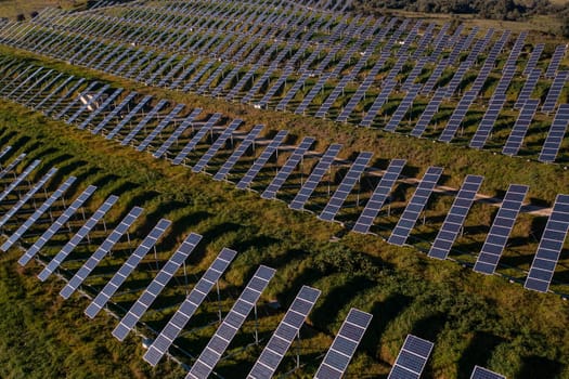 Aerial view flying over a solar panel farm at summer day with industrial city area on background, the future of green renewable energy is the sun