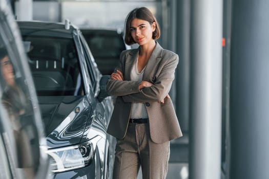Black colored car. Woman is indoors near brand new automobile indoors.