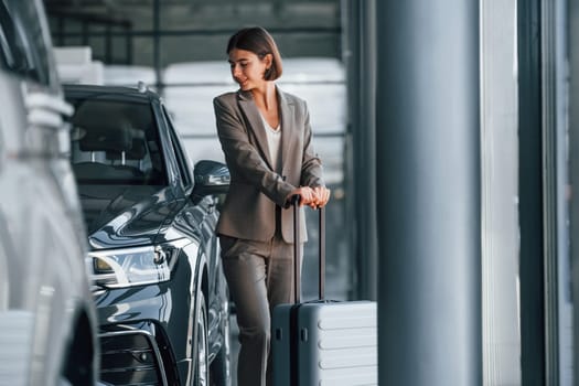 Posing for a camera. Woman is indoors near brand new automobile indoors.