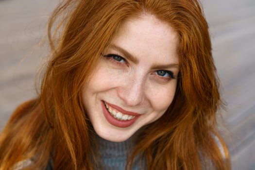 female closeup portrait, caucasian red-haired cute young woman with freckles and green eyes looks into the frame and cute smiling