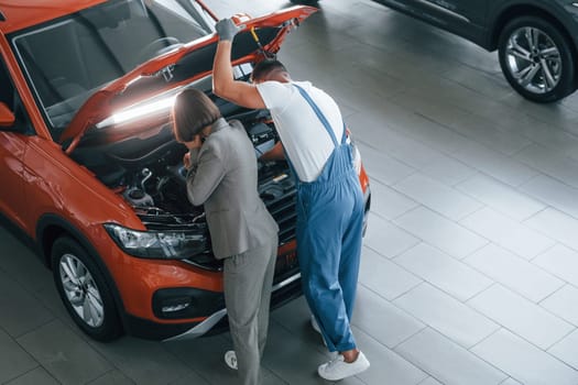 Owner standing near the man that repairing automobile indoors. Professional service.