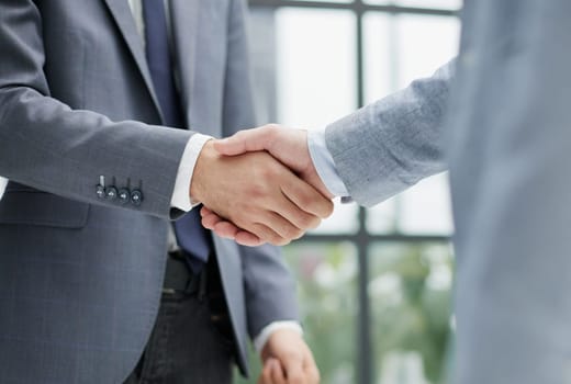 Businessmen shake hands, standing near a large office window