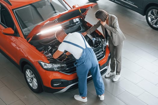 Owner standing near the man that repairing automobile indoors. Professional service.