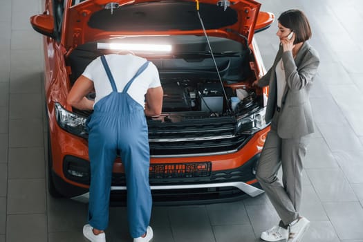 Owner standing near the man that repairing automobile indoors. Professional service.