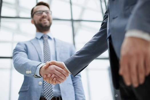 Businessmen shake hands, standing near a large office window