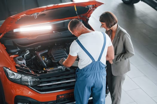 Woman in stylish clothes. Man repairing woman's automobile indoors. Professional service.
