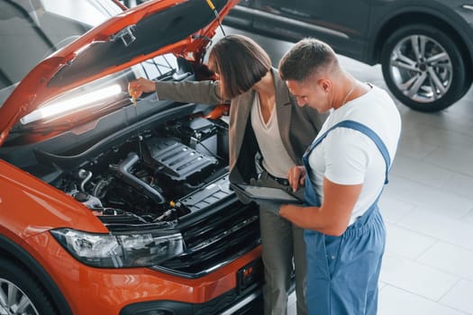 Woman in stylish clothes. Man repairing woman's automobile indoors. Professional service.
