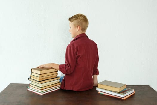 Education concept. Pupil boy sits at the table with his back to the camera, next to the books.