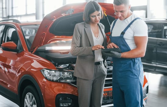 Woman in stylish clothes. Man repairing woman's automobile indoors. Professional service.