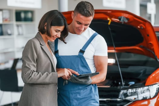 Paying for service. Man repairing woman's automobile indoors.