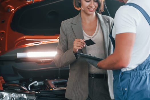 Paying for service. Man repairing woman's automobile indoors.