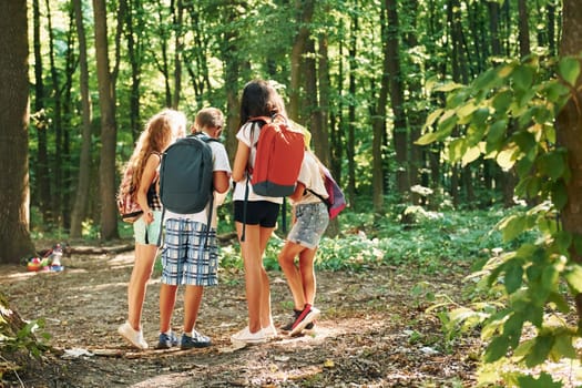 Kids strolling in the forest with travel equipment.