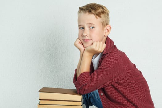 A schoolboy sits on the table near the books, leaning his elbows on them and looks into the cameras. Education concept