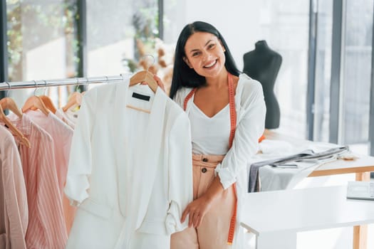 Standing and smiling. Seamstress is in her office that is with different clothes.