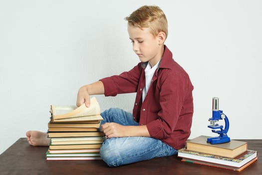 Schoolboy sitting at the table near the books and leafing through the pages of the book. Education concept