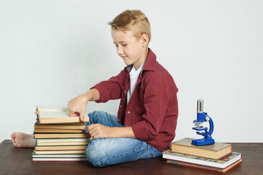 Schoolboy sitting at the table near the books and leafing through the pages of the book. Education concept