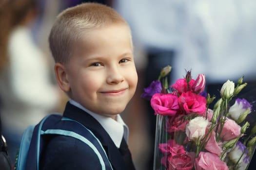 a fair-haired little boy, a schoolboy, with a bouquet of bright flowers smiles and looks at the camera. The first of September is the day of knowledge