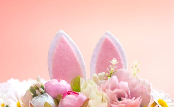 Spring holidays creative background with bunny ears decorated with bloom flowers on pastel pink theme. Creative copy space Easter concept space for text