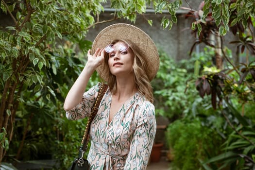 cute young blonde woman posing and smiling among the greenery in the greenhouse