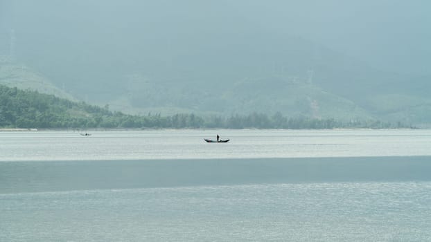 A boat with a fisherman in the middle of the river against the backdrop of foggy mountains. High quality photo