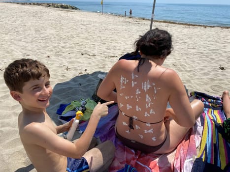 Smiling young boy applying sunscreen on his mother shoulder in the beach