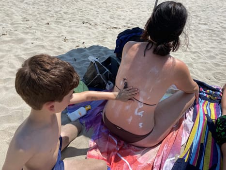 Smiling young boy applying sunscreen on his mother shoulder in the beach