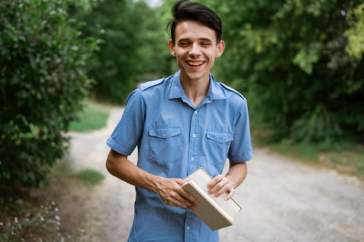 Student guy in a blue shirt with a book in his hand in the park reads