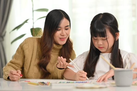 Happy asian mother and little daughter coloring a picture, doing a hobby or education project together at home.