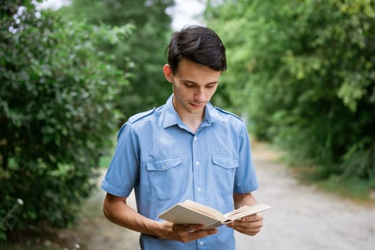 Student guy in a blue shirt with a book in his hand in the park reads