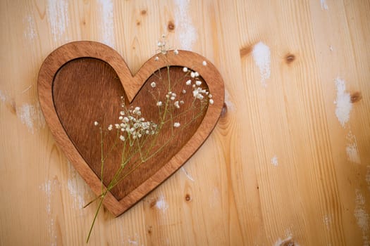 wooden heart with a sprig of small white flowers lies on a wooden background