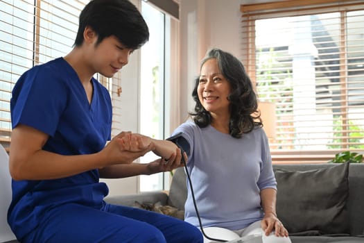 Young male healthcare worker measuring blood pressure middle age woman during home visit. Home health care service concept.