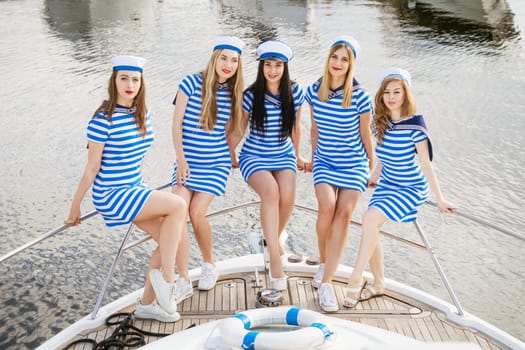 Cheerful girlfriends in striped dresses and shirts on a yacht in the summer. Happy young women of Caucasian appearance are resting. Tourism and travel concept